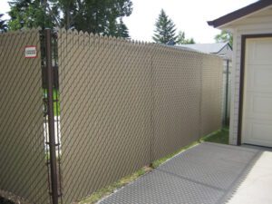 Tan privacy insert chain link residential fence in Winnipeg along driveway between suburban homes
