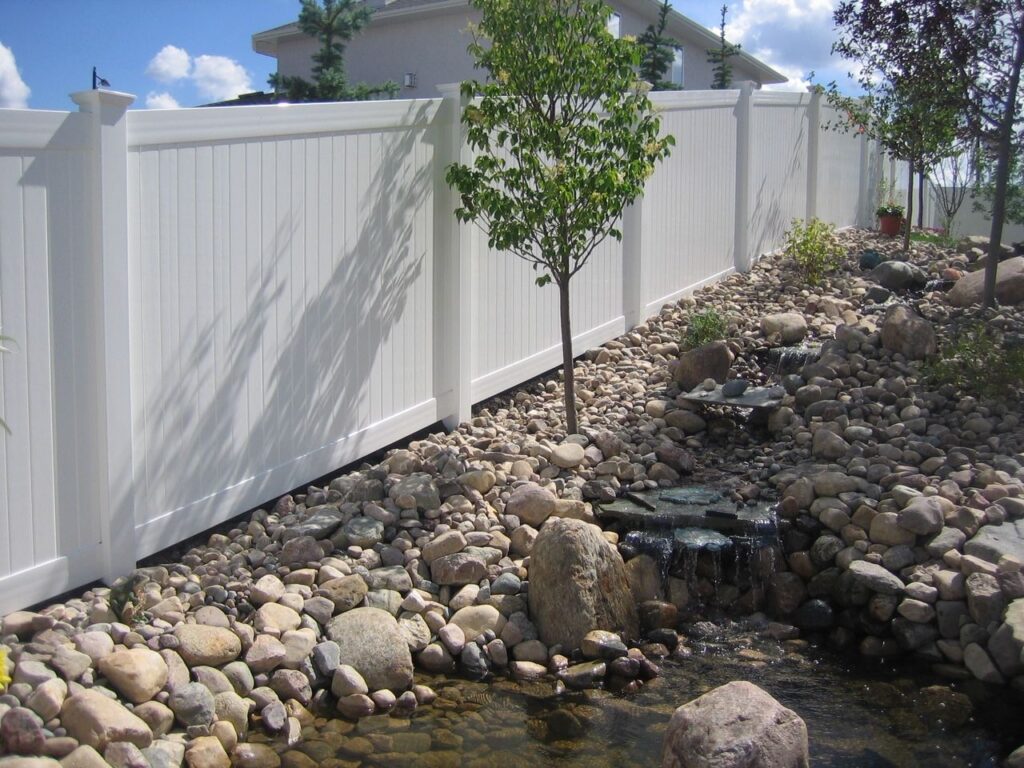 White Vinyl Fencing in Winnipeg bordering rock garden with waterfall feature and young tree