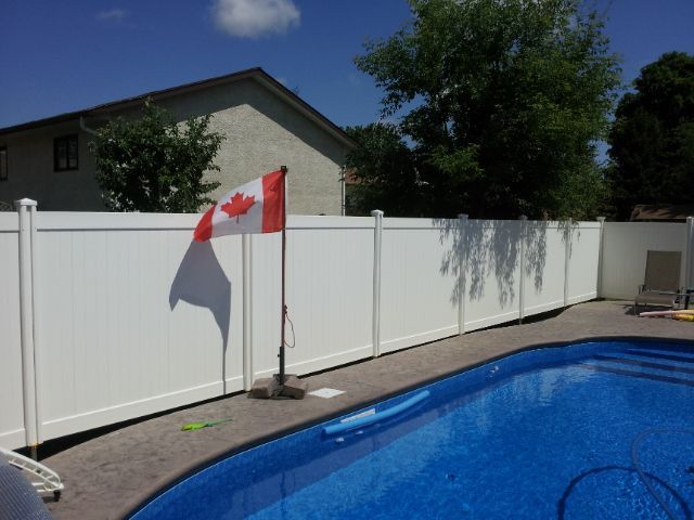 Tall white vinyl fence surrounding backyard pool with Canadian flag.